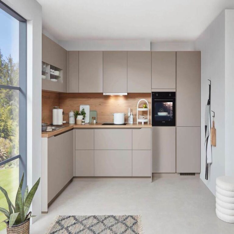 Musterküche in Kaschmir Musterküche in Kaschmir als L-Küche mit Holzrückwand und Backofen im Hochschrank – Küchenidee